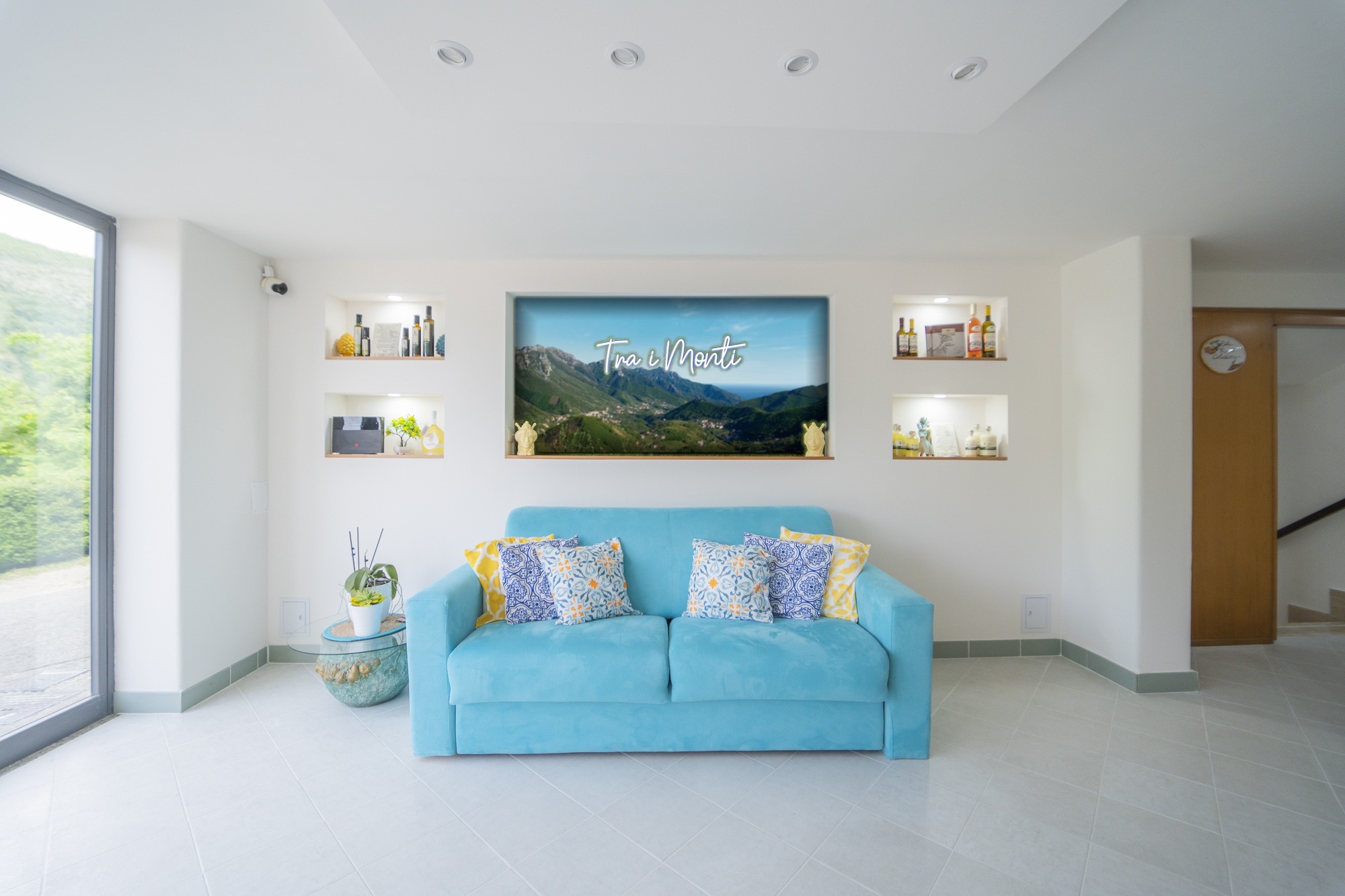 La reception con il divano azzurro e, alle spalle, la parete con il panorama della valle di Tramonti e la scritta luminosa Tra i Monti